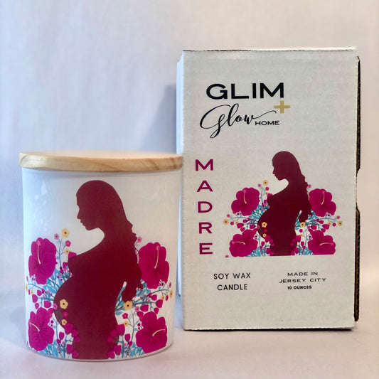 Soy candle in white jar with woman in center surrounded by flowers. Candle is called Madre and is a donation candle
